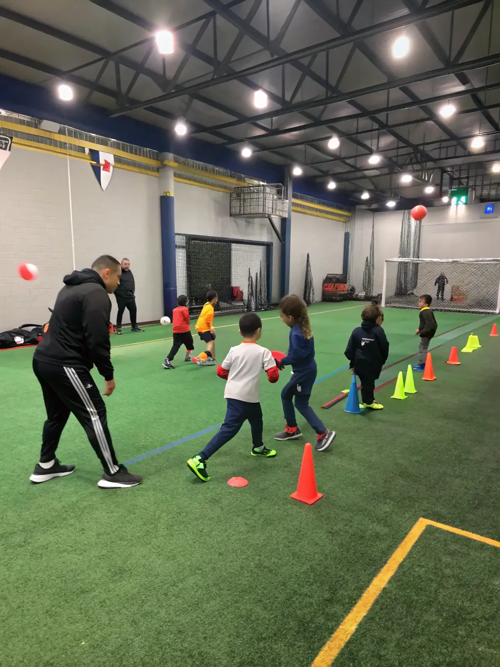 A group of children and teenagers participating in a multi-sport workshop in a modern gymnasium, with coaches guiding them through various athletic activities, representing youth engagement and skill development.